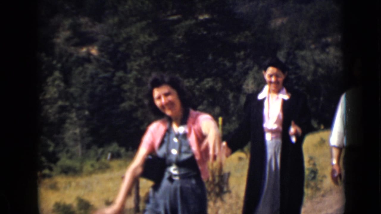Women in dresses and cardigans walk toward the camera on a rural roadside.