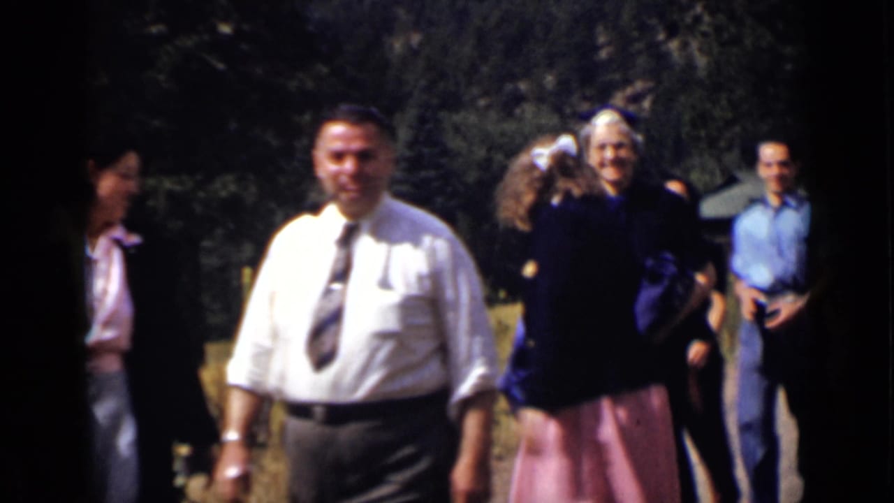 A man in a white shirt and tie walks ahead of a small dressed group outdoors.