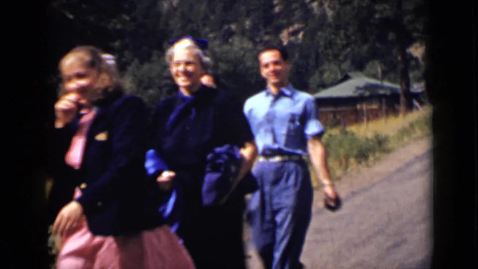 Adults walk casually along a rural road in Colorado, including two women in dark jackets and a man in blue clothing.