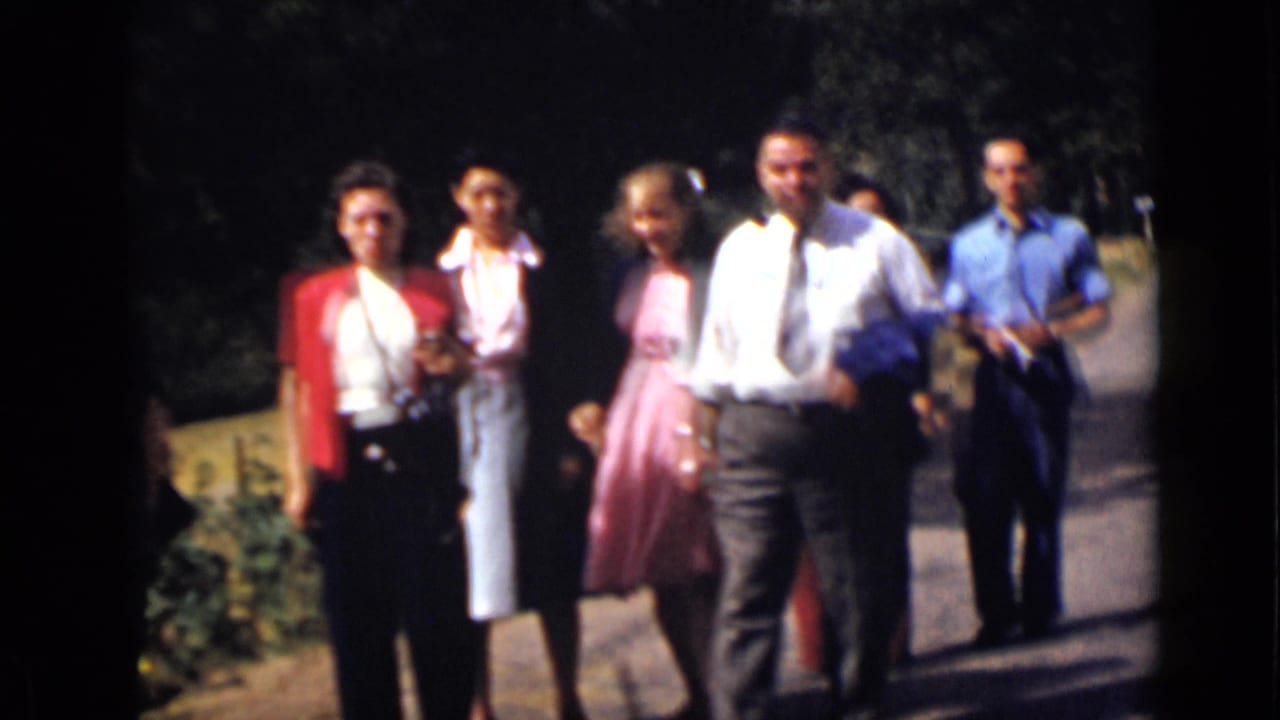 Adults walk toward the camera on a sunny tree-lined path.