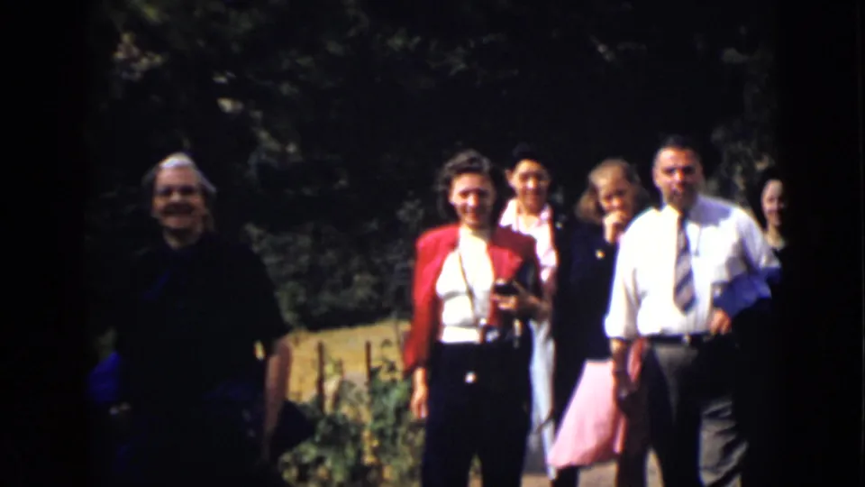 A smiling adult group walks toward the home-movie camera in a Colorado park or garden setting.
