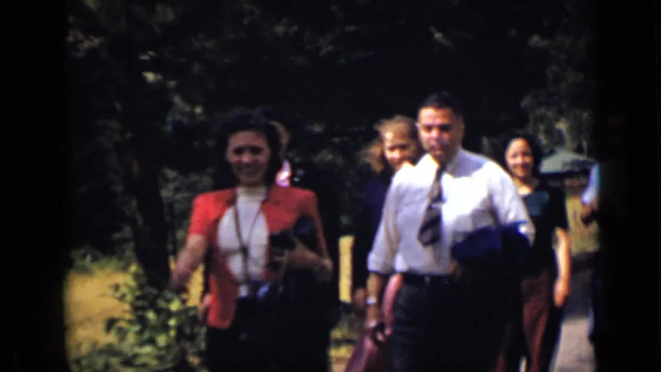 Several adults in period clothing pass close to the camera on a sunlit Colorado path with trees behind them.