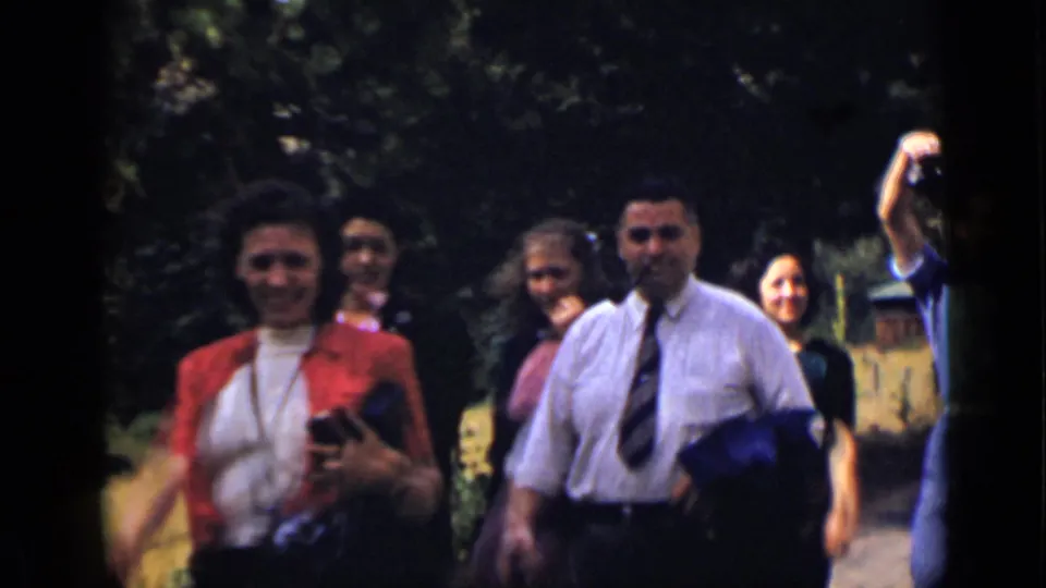 In 1939 Colorado home-movie footage, adults walk toward the camera in a wooded area, including a woman in red holding a camera.