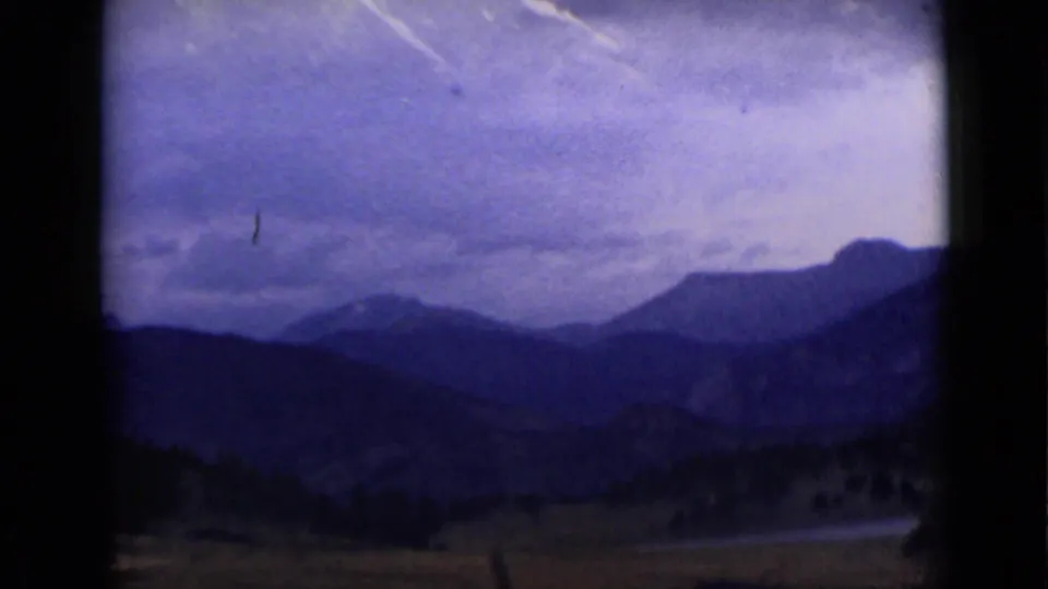 1939 Colorado 8mm landscape frame showing dark mountain ridges, a valley, cloudy sky, and a small light-toned water or road feature.
