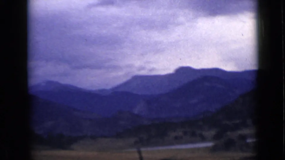 1939 Colorado scenic frame with layered blue mountain ridges, a valley floor, cloudy sky, and soft handheld 8mm framing.