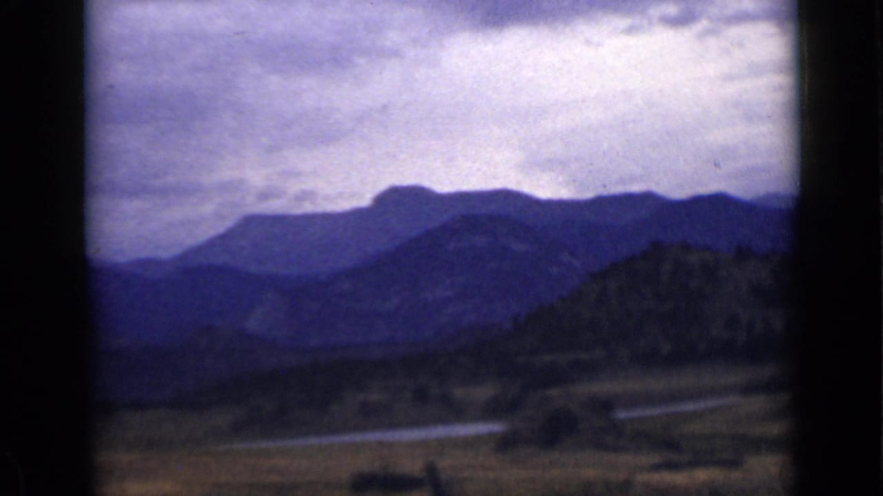 Layered blue mountain ridges under a cloudy sky with river and trees in the foreground.