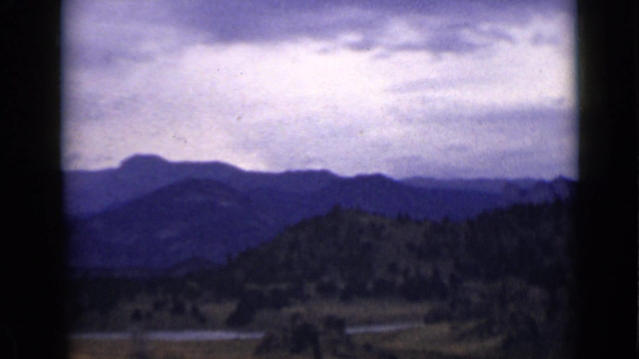 Blue mountain range and wooded hill above a pale winding waterway.