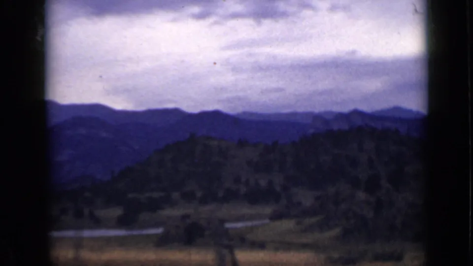 1939 Colorado 8mm still with soft blue ridges, a tree-covered hill, open valley ground, and a narrow river segment.