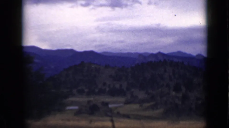 Colorado mountain landscape on 1939 8mm film, showing blue ridgelines, a wooded hill, open valley terrain, and visible film wear.