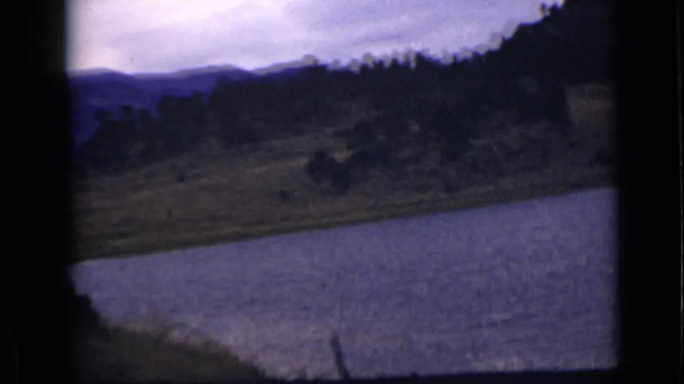 Colorado landscape view from a moving vehicle, with blue-toned water, wooded slopes, and distant mountains.