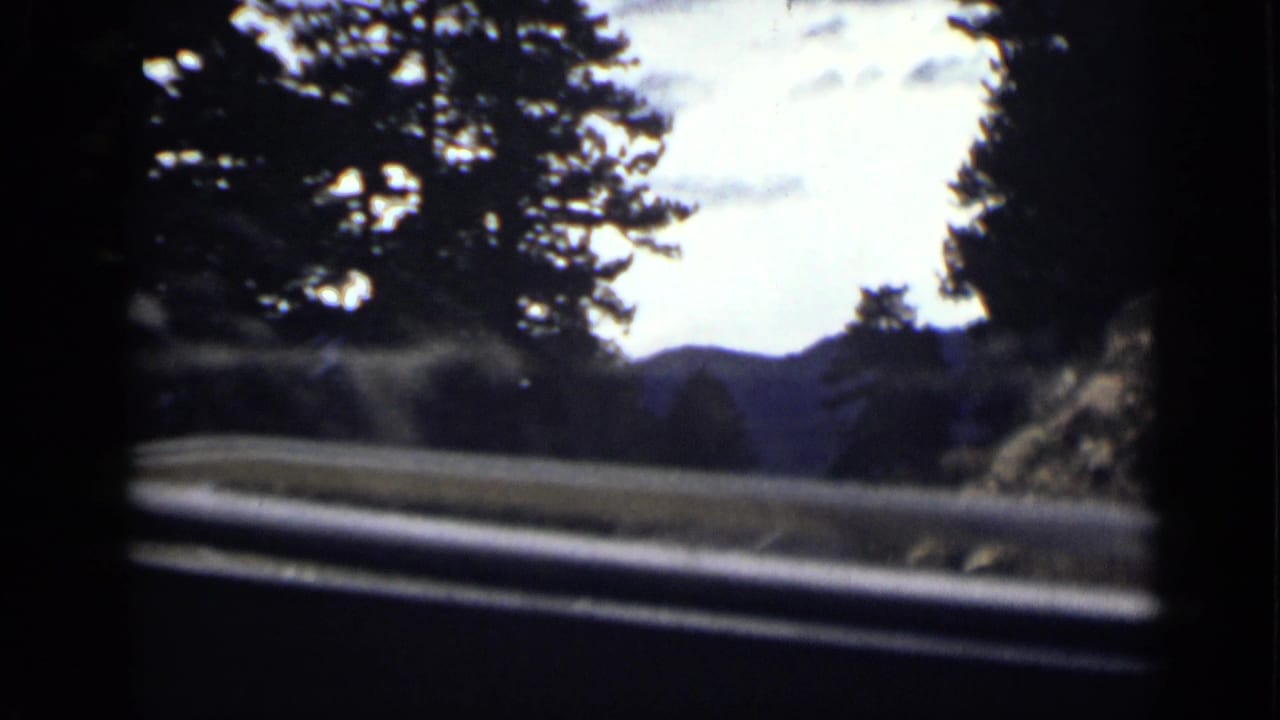 1939 Colorado 8mm frame showing a passenger view through a windshield toward a guarded mountain road and tree-lined hills.
