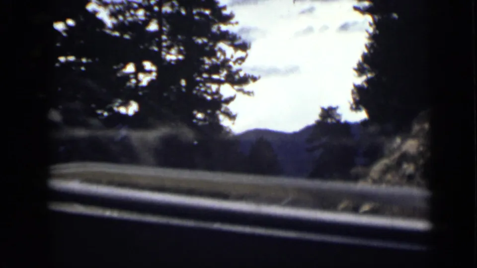 1939 Colorado 8mm frame showing a passenger view through a windshield toward a guarded mountain road and tree-lined hills.