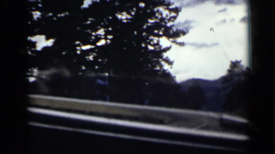 Colorado mountain road view from inside a moving vehicle, with guardrail, evergreens, and hazy hills visible through the windshield.