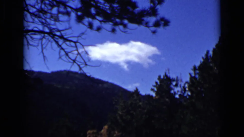 Colorado mountain landscape on 8mm film, with evergreen trees in shadow and a white cloud above the ridge.