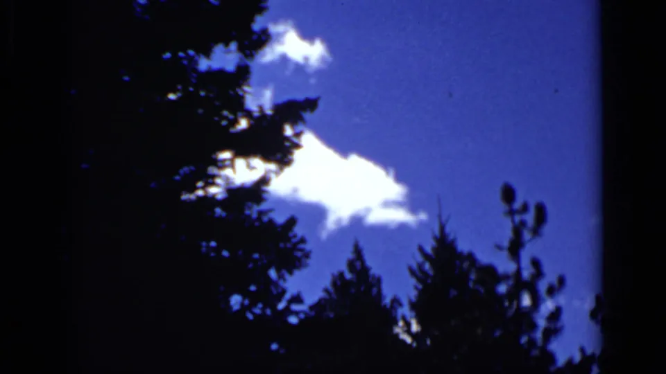8mm Colorado landscape frame with dark evergreen silhouettes and a bright cloud dominating the blue sky.