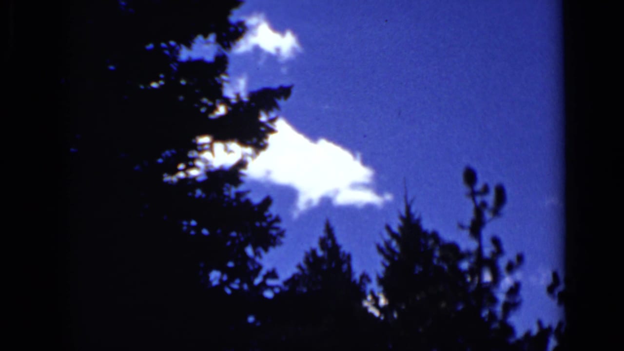 1939 Colorado 8mm frame showing deep blue sky, white clouds, and dark conifer silhouettes at the edge of the film frame.