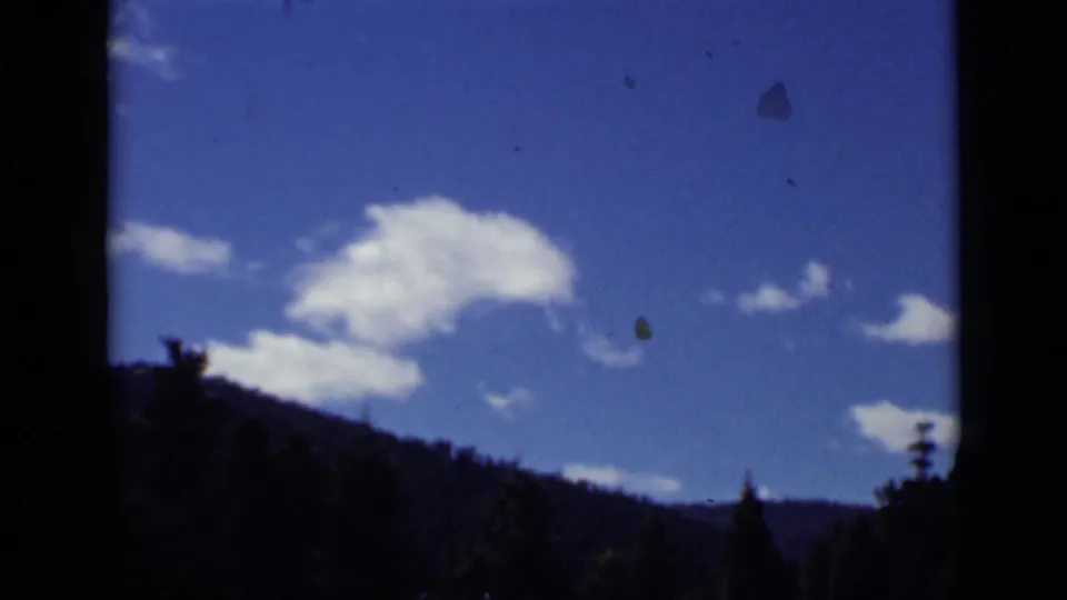 1939 Colorado mountain-sky cutaway showing scattered white clouds above a forested ridge on color 8mm film.