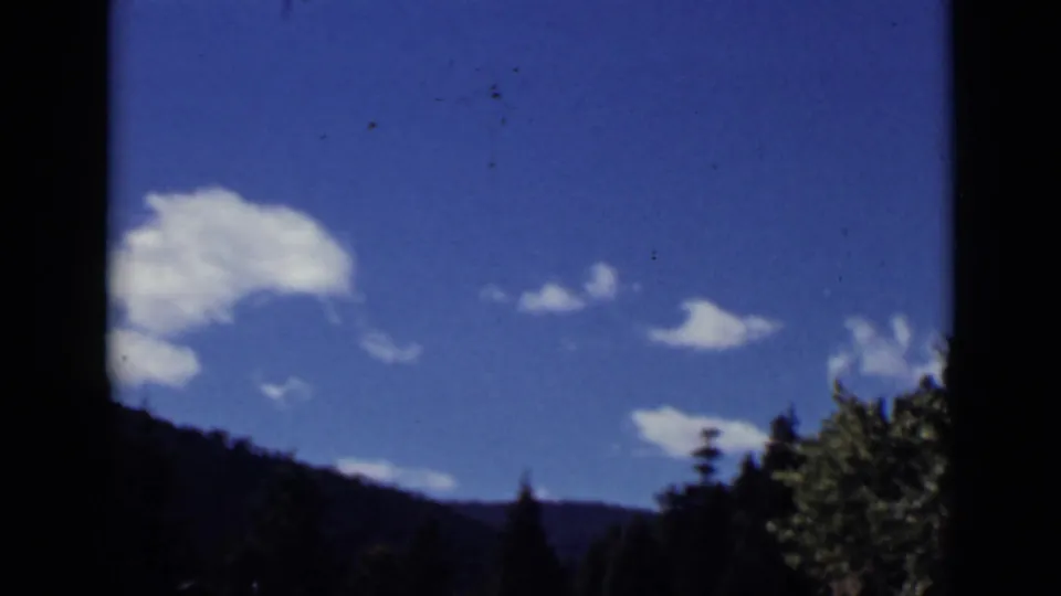 1939 Colorado home-movie view of bright clouds over a wooded ridge, seen through dark vertical framing.