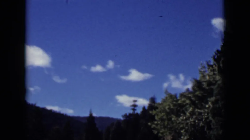 Colorado 8mm frame from 1939 showing blue sky, scattered clouds, and a shadowed tree-covered hillside.