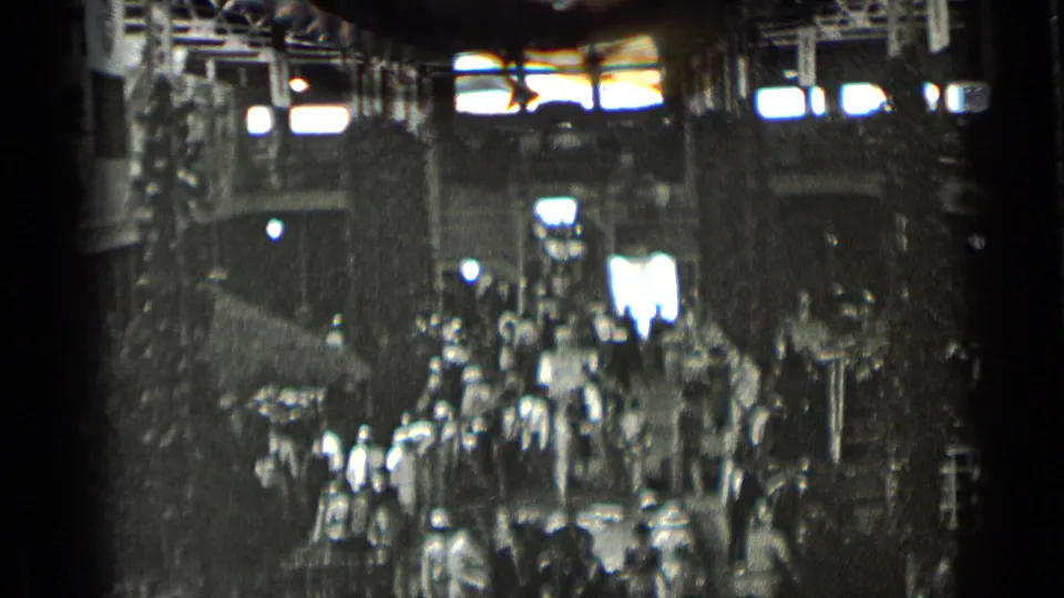 1939 New York 8mm frame showing a crowded indoor public hall with high windows, columns, and people moving below.