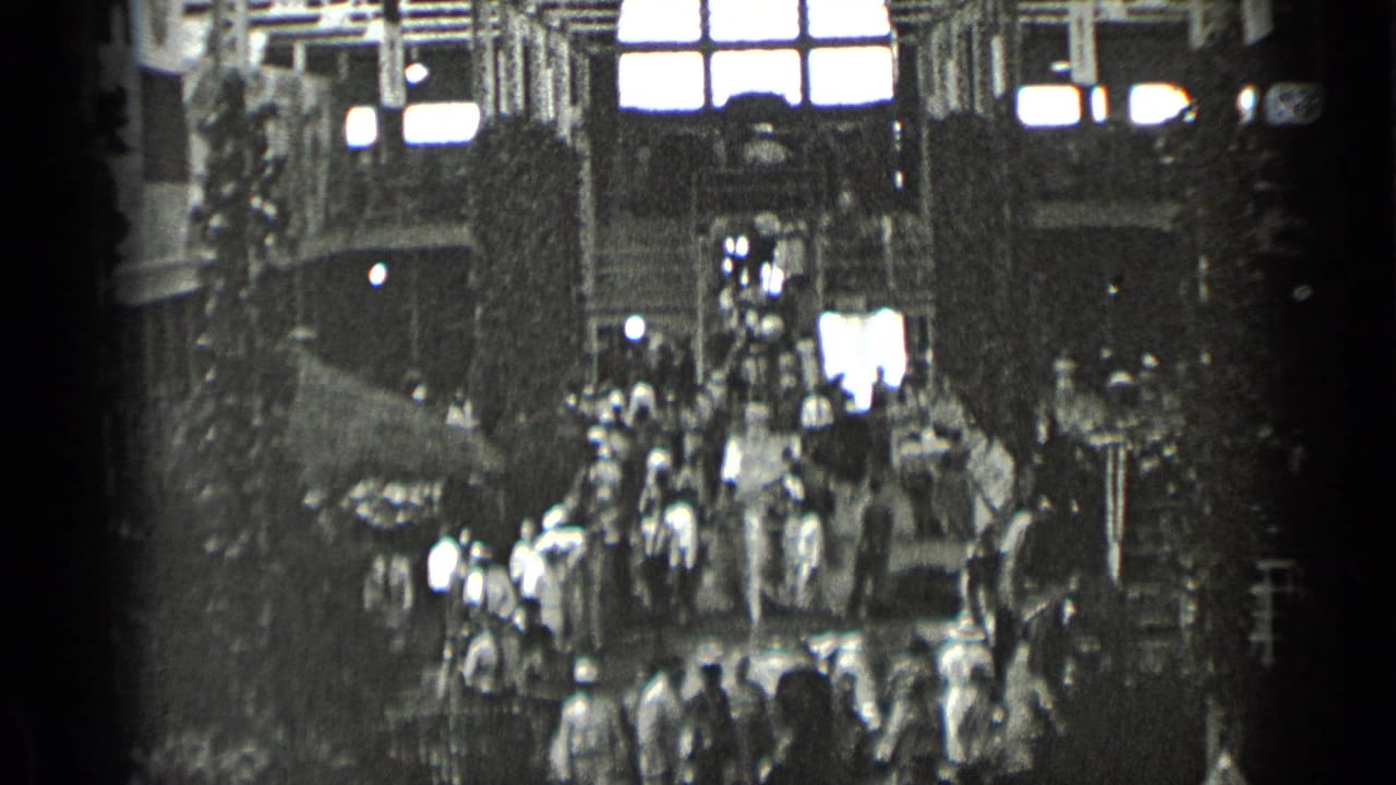 1939 New York 8mm frame showing a bustling public interior, with people crossing beneath tall windows and heavy structural framing.