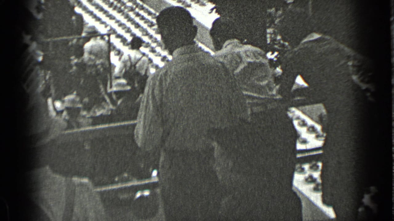 People standing near a building entrance, seen in grainy black-and-white footage.