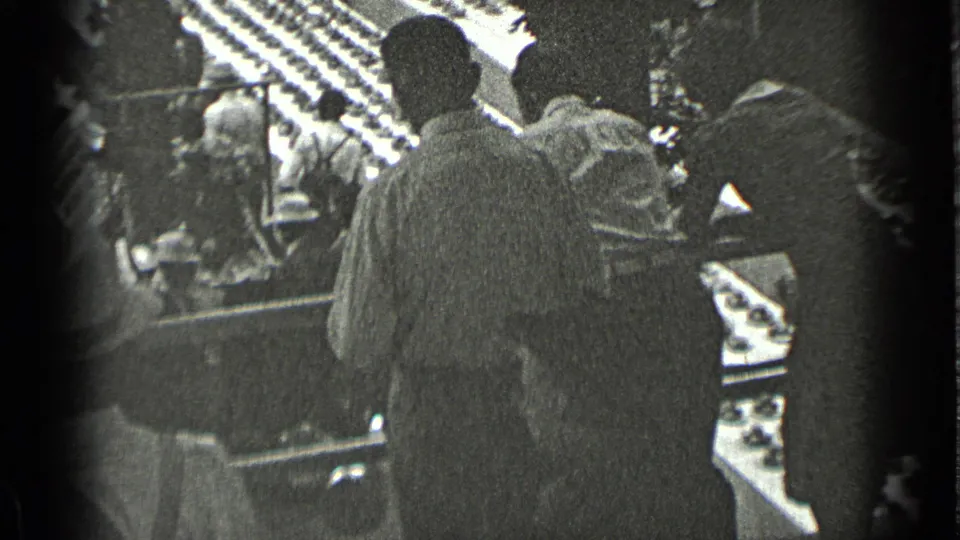 A 1939 New York 8mm frame appears to show people gathered near an exterior building entrance with awning-like shapes and deep shadow.