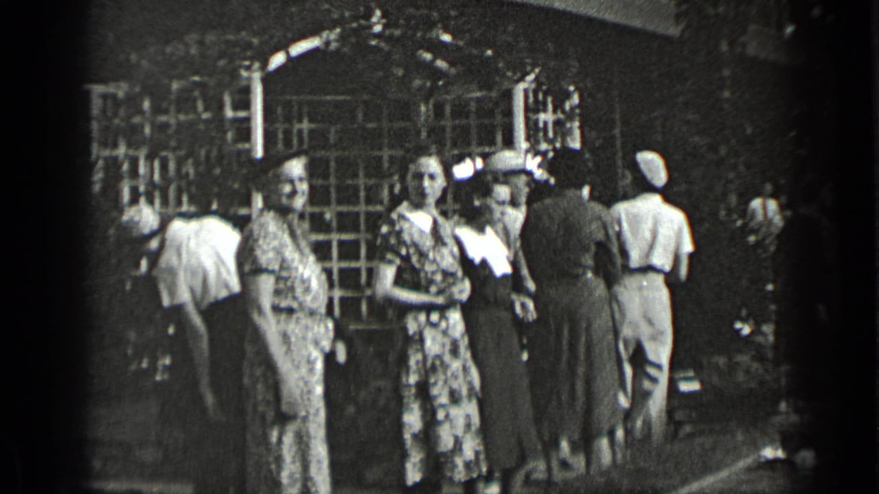 Women in late-1930s-style dresses and hats stand outside a New York building with a latticed archway while other adults move nearby.