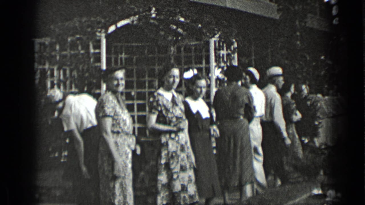 A New York 1939 home-movie frame shows women in patterned dresses near a building entrance, with men and women passing in the background.