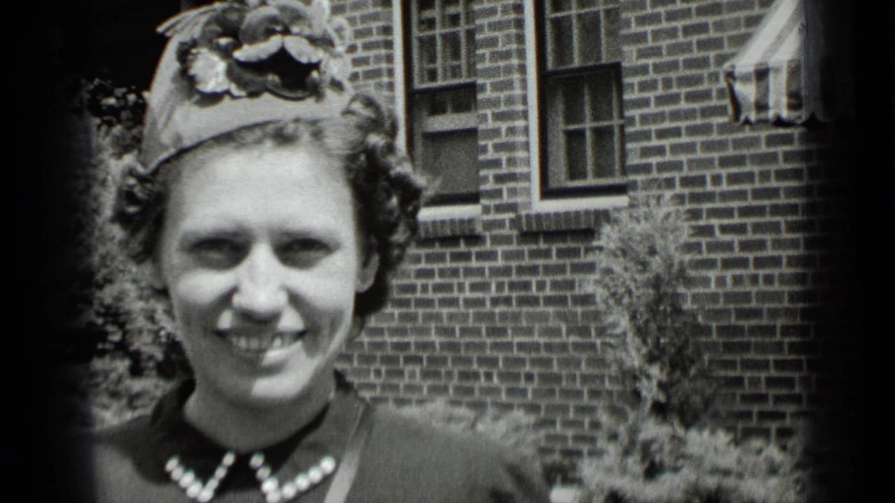 Woman in a decorative hat smiles outdoors in front of a brick building.