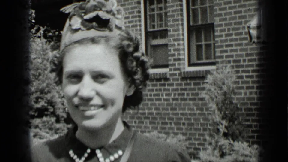 A close 1939 New York frame shows the woman smiling broadly, with her hat, curled hair, and pearl-trimmed collar visible.