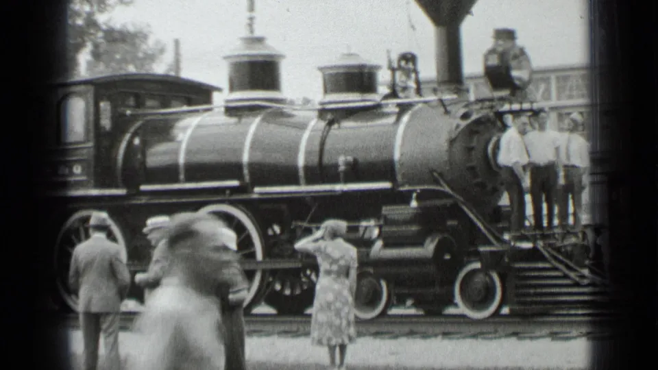 A steam locomotive stands at a New York rail platform in the 1939 home movie, with people gathered near the engine and steps.
