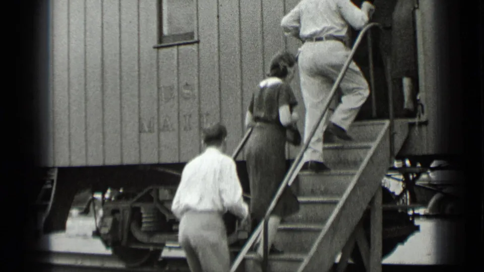 In 1939 New York footage, men and a woman board a wooden U.S. Mail train car by metal steps.