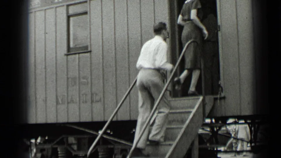 A man in a light shirt and trousers follows a woman up metal steps into the train car.