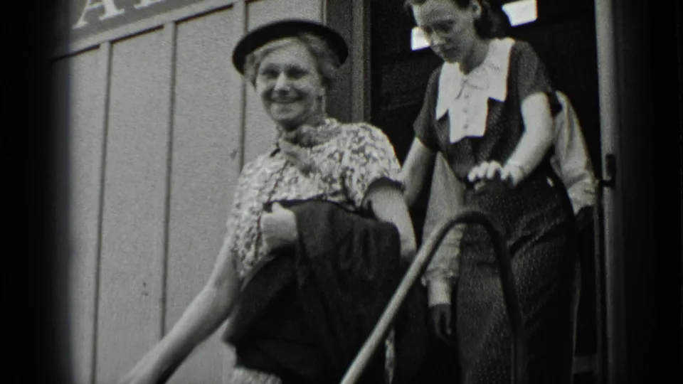 A smiling woman in a hat leaves a fair ride in New York, followed by a younger woman in a dark dress with a white collar.