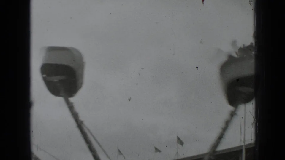 1939 New York home-movie frame showing blurred fairground structures, small flags, and heavy 8mm gate edges.