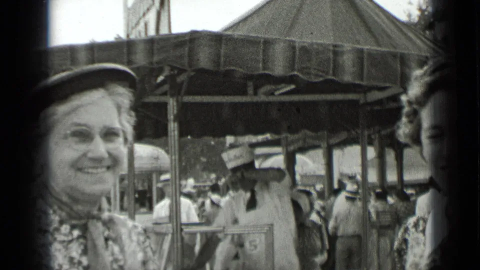 1939 New York fair frame with a smiling woman in a hat facing the camera as visitors move under a canopy.