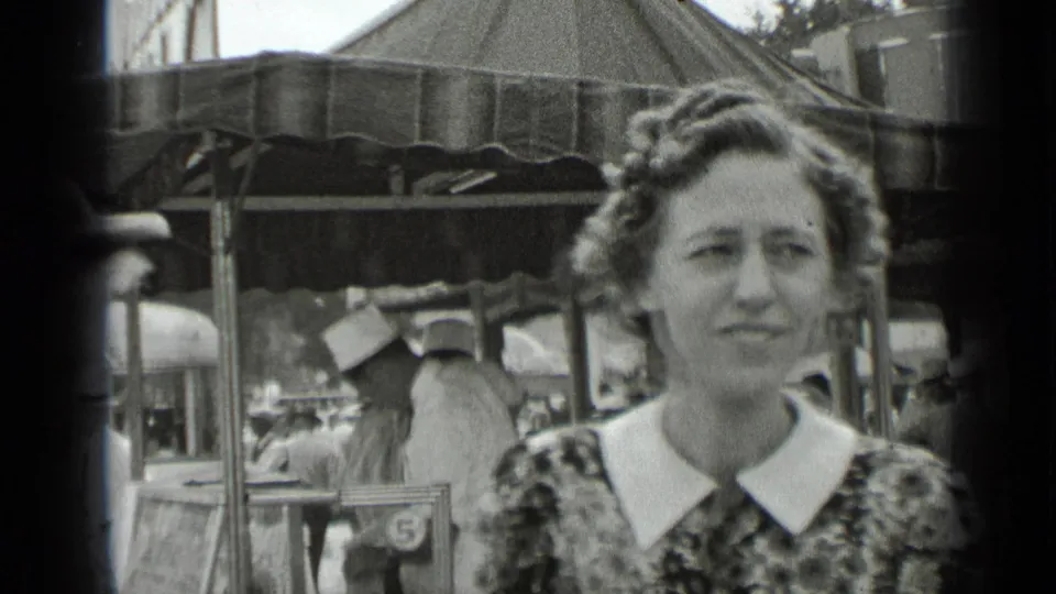 A woman with curled hair and a wide white collar looks toward the camera near a crowded 1939 New York fair stall.