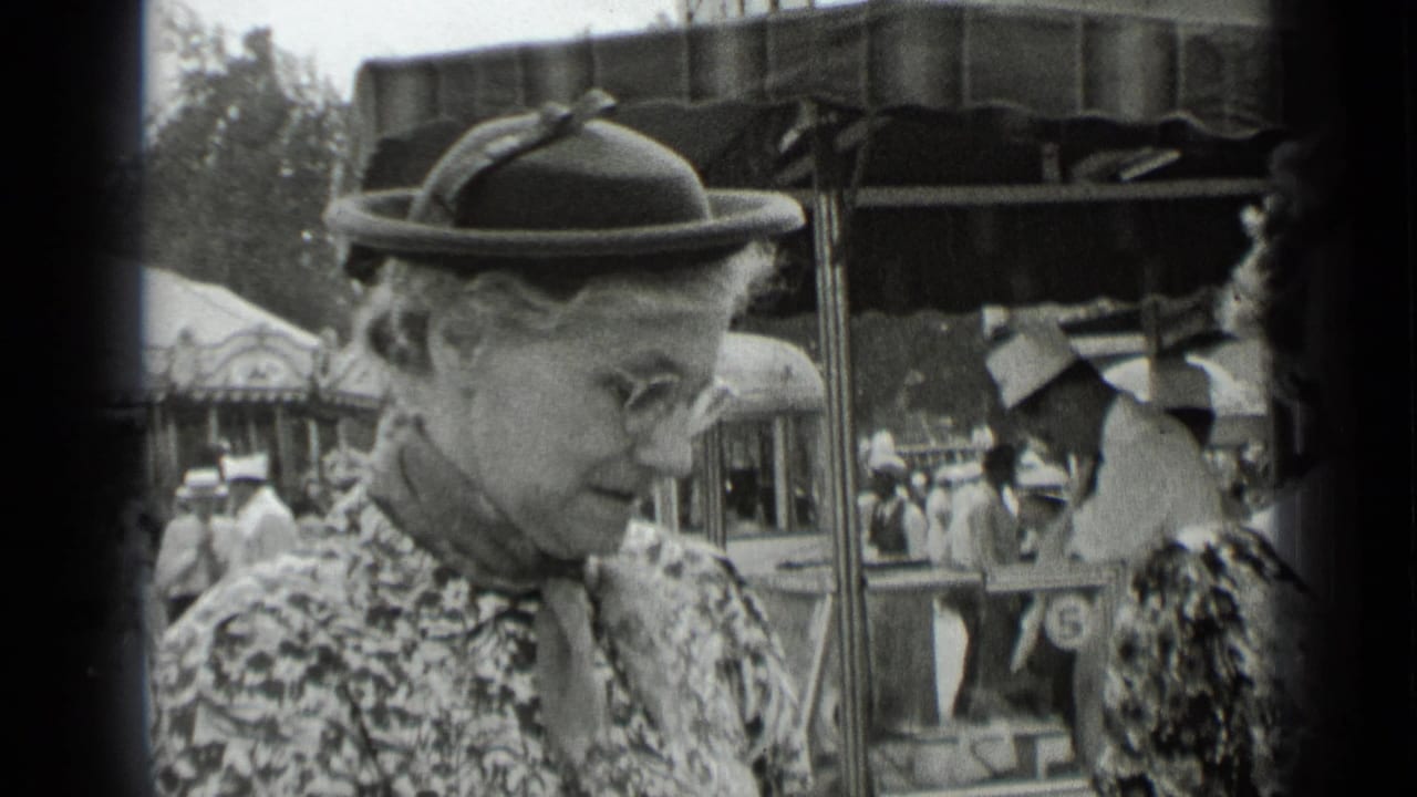 Older woman in a brimmed hat stands near fair structures and passing visitors.