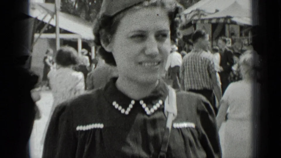 The same young woman smiles in soft-focus black-and-white footage, with 1939 New York fair visitors and structures visible behind her.