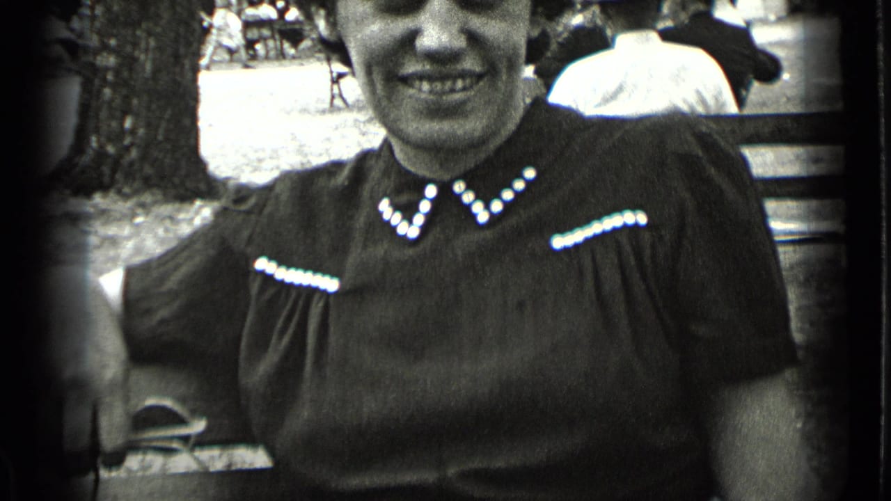 Smiling woman seated on a park bench in a dark dress with white beaded trim.