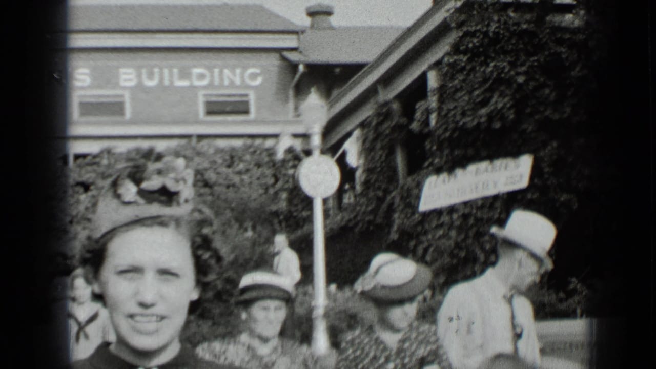 Crowd in hats near a building with a partial sign and leafy wall.
