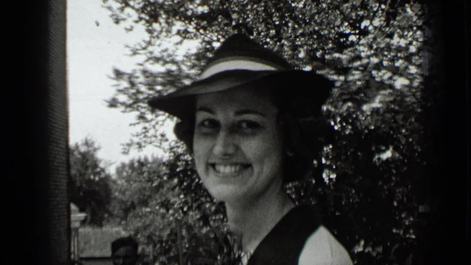 1939 New York home-movie close-up of a smiling woman in a wide-brimmed hat, with trees and a path behind her.