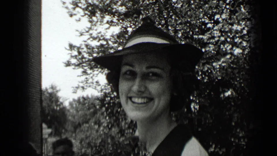 1939 New York home-movie close-up of a woman smiling beneath a wide-brimmed hat, framed by leafy branches.
