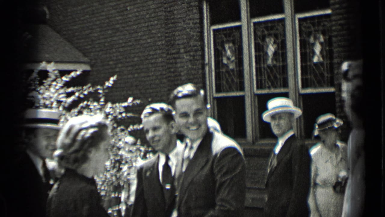 Smiling men and women in formal clothing stand near shrubs and brick windows.