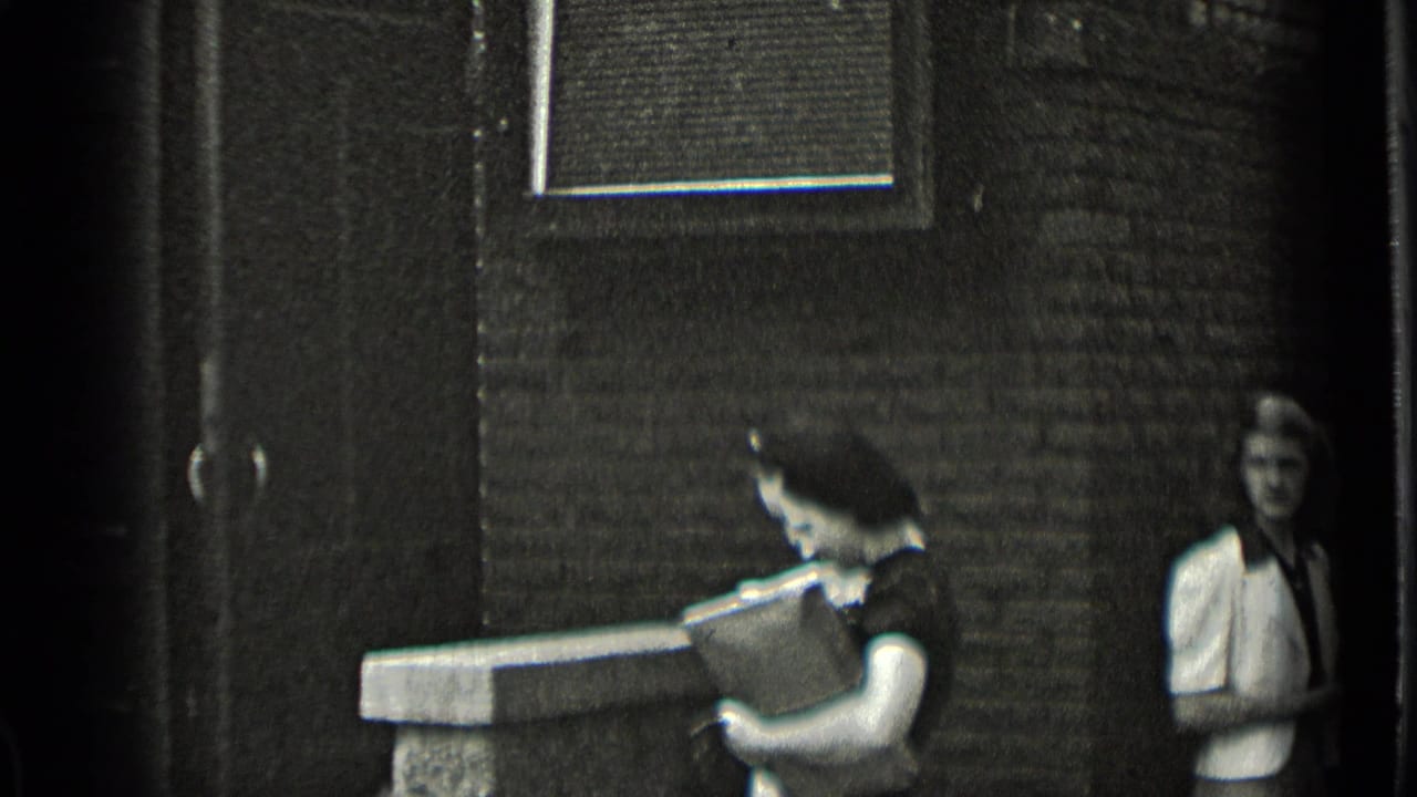 Two women near a brick building entrance, one carrying a rectangular case.