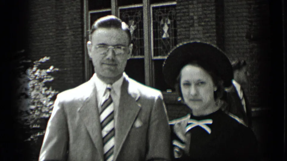 A dressed man and woman face the camera in 1939 New York home-movie footage, framed by brickwork and decorative windows.