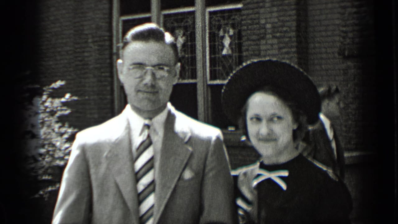 Man in suit and woman in dark dress pose outside a brick building.