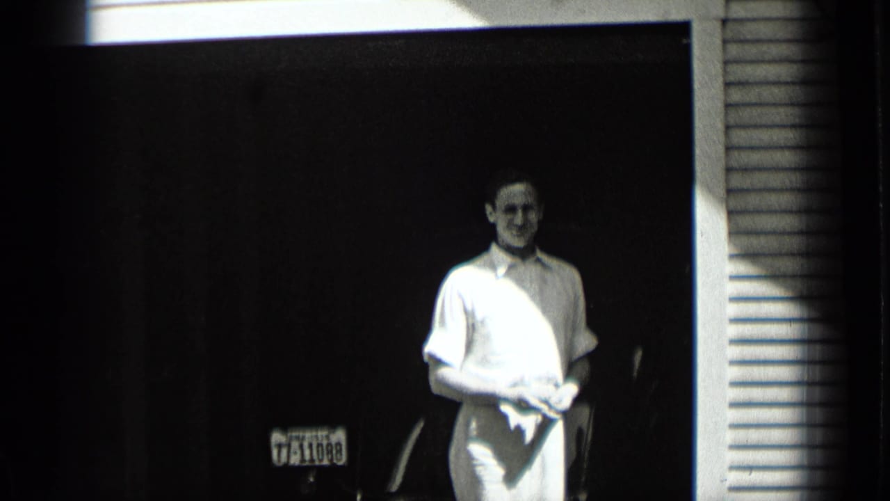 The man remains framed in the doorway in this 1939 New York clip, facing the camera with a cloth in his hands and a license plate behind him.