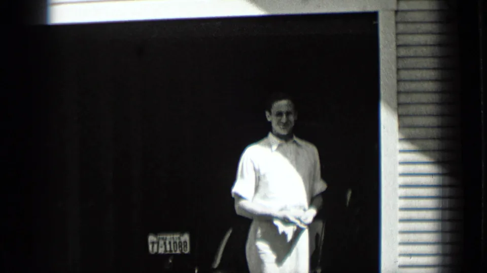 The man remains framed in the doorway in this 1939 New York clip, facing the camera with a cloth in his hands and a license plate behind him.
